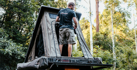 Person in an open rooftop tent at camp