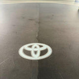 A clear vinyl decal of the Toyota logo applied to the glossy black hood of a vehicle.